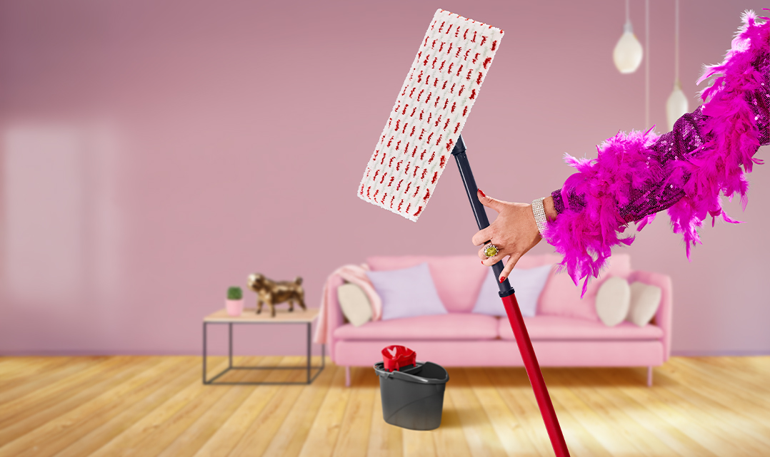 En arm i en pailletjakke og en fjerboa holder en Vileda-moppe i en farverig stue.